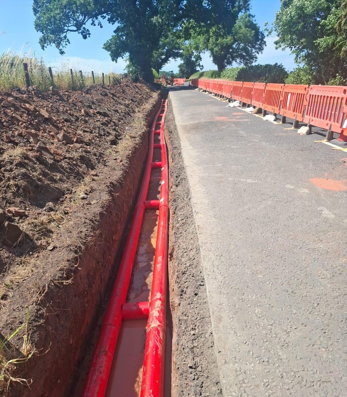 Twin HV ducts in trench beside a tarmac road with pedestrian barriers