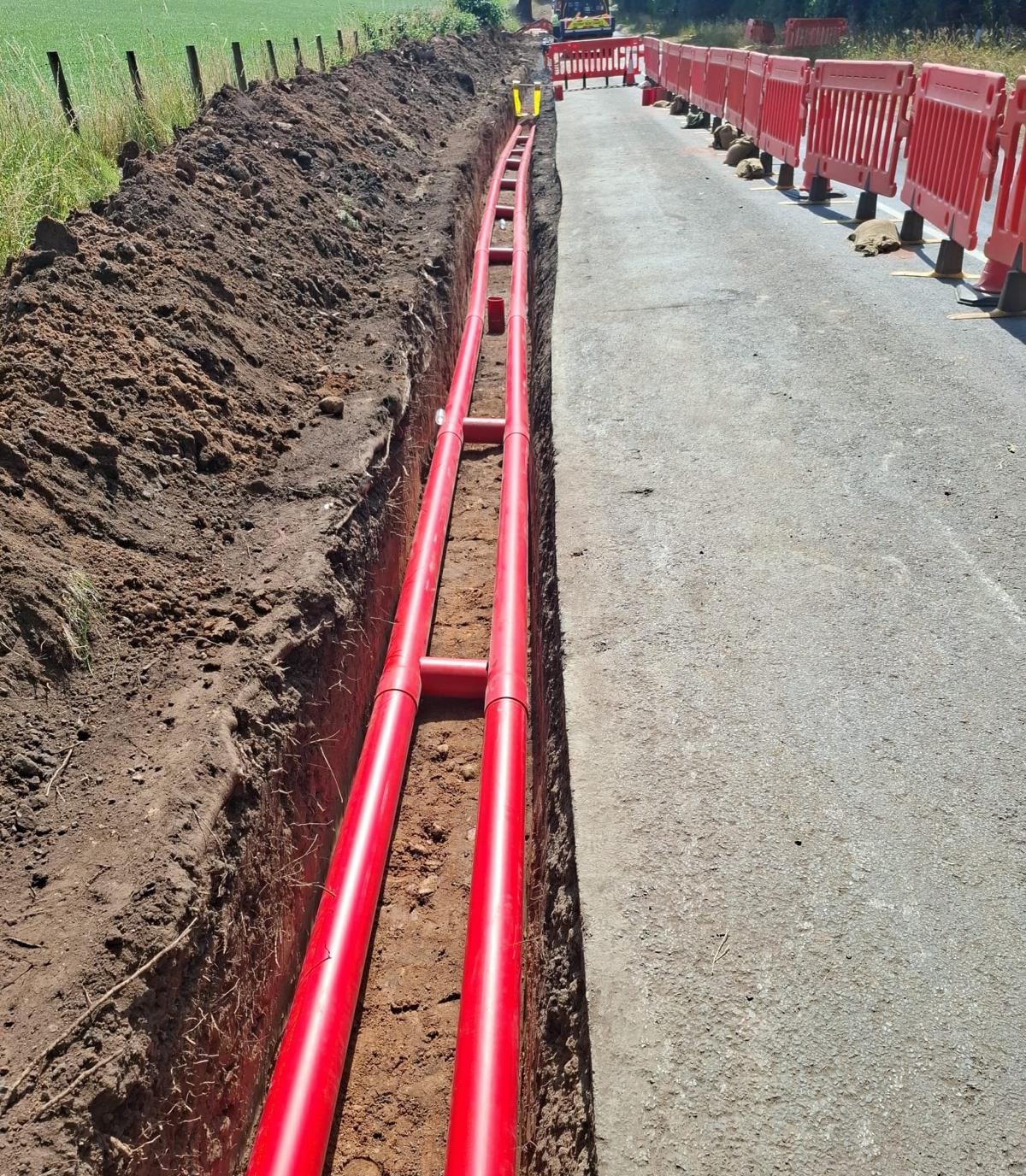 Twin red HV ducts laid in an open trench along a rural road